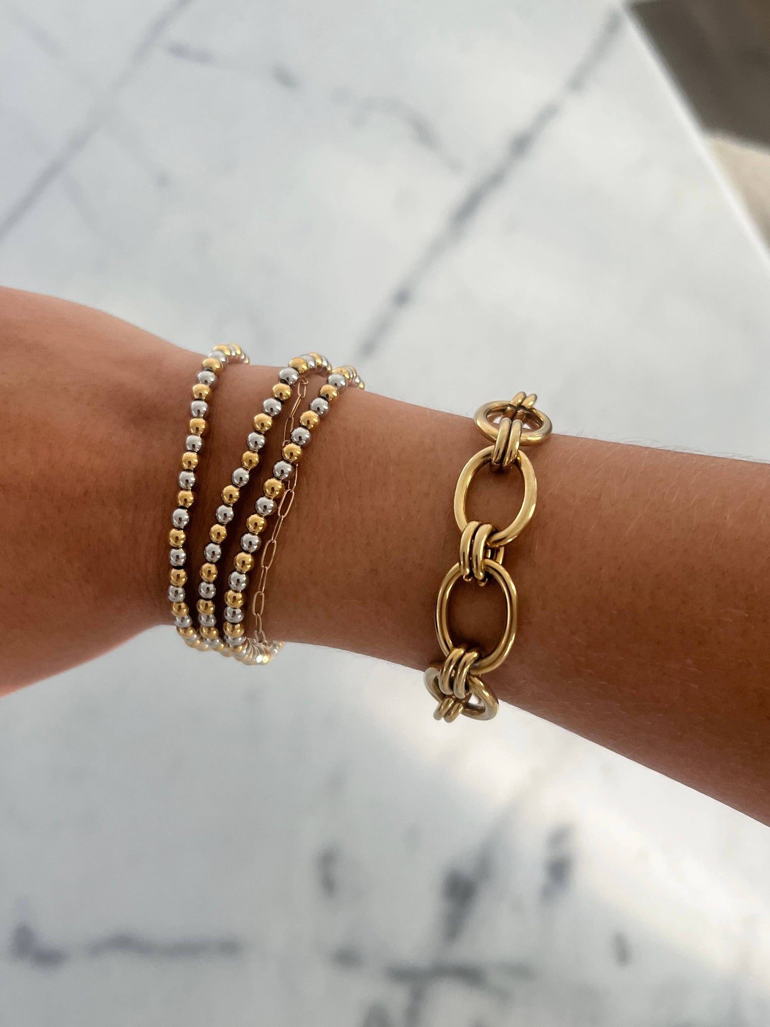 Gold bracelets on a wrist with a marble background